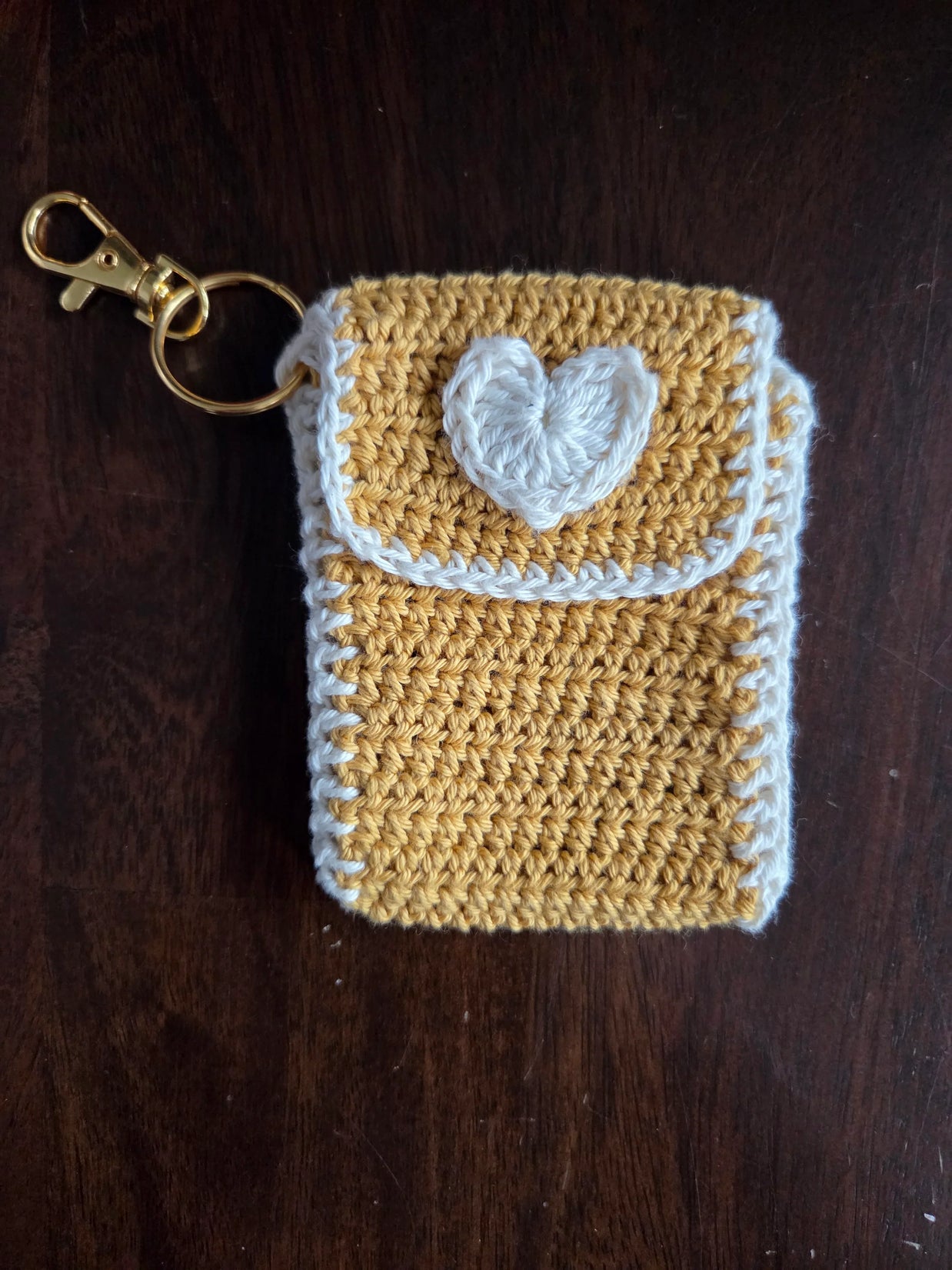 Handmade yellow crochet keychain pouch with white heart on wooden background