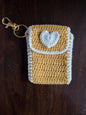 Handmade yellow crochet keychain pouch with white heart on wooden background