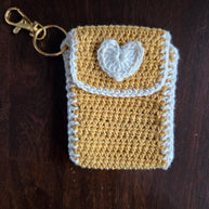 Handmade yellow crochet keychain pouch with white heart on wooden background