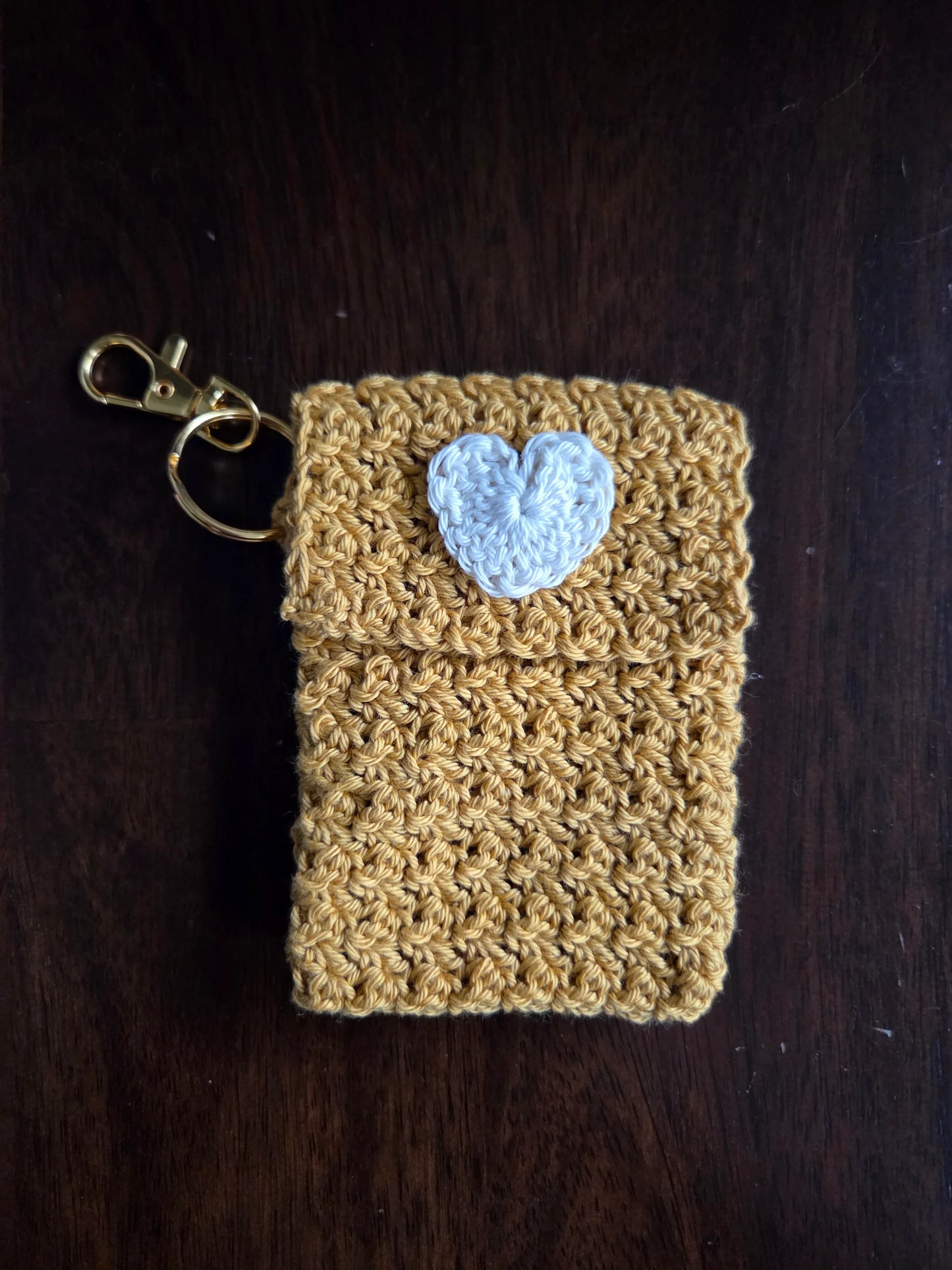 Yellow crochet keychain pouch with white heart on dark wood background