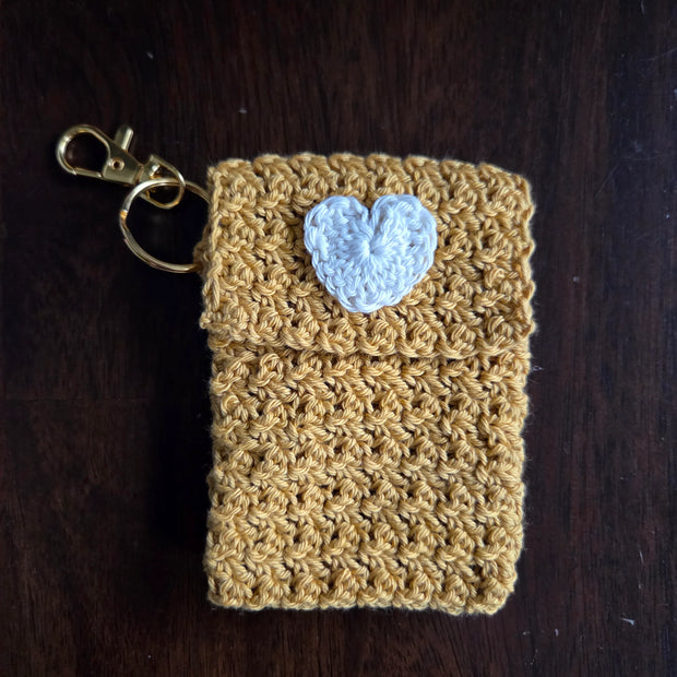 Yellow crochet keychain pouch with white heart on dark wood background