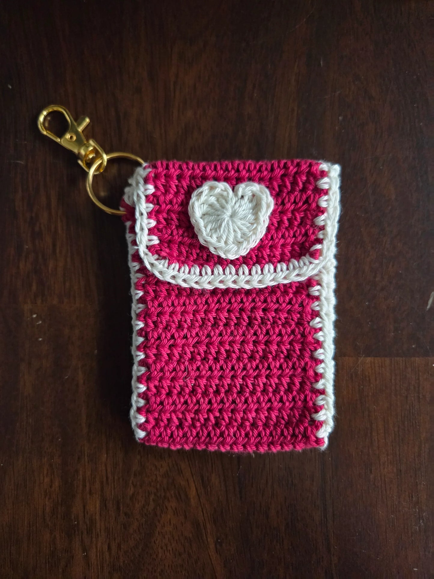 Handmade pink crochet keychain pouch with white heart on wooden surface