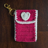Handmade pink crochet keychain pouch with white heart on wooden surface