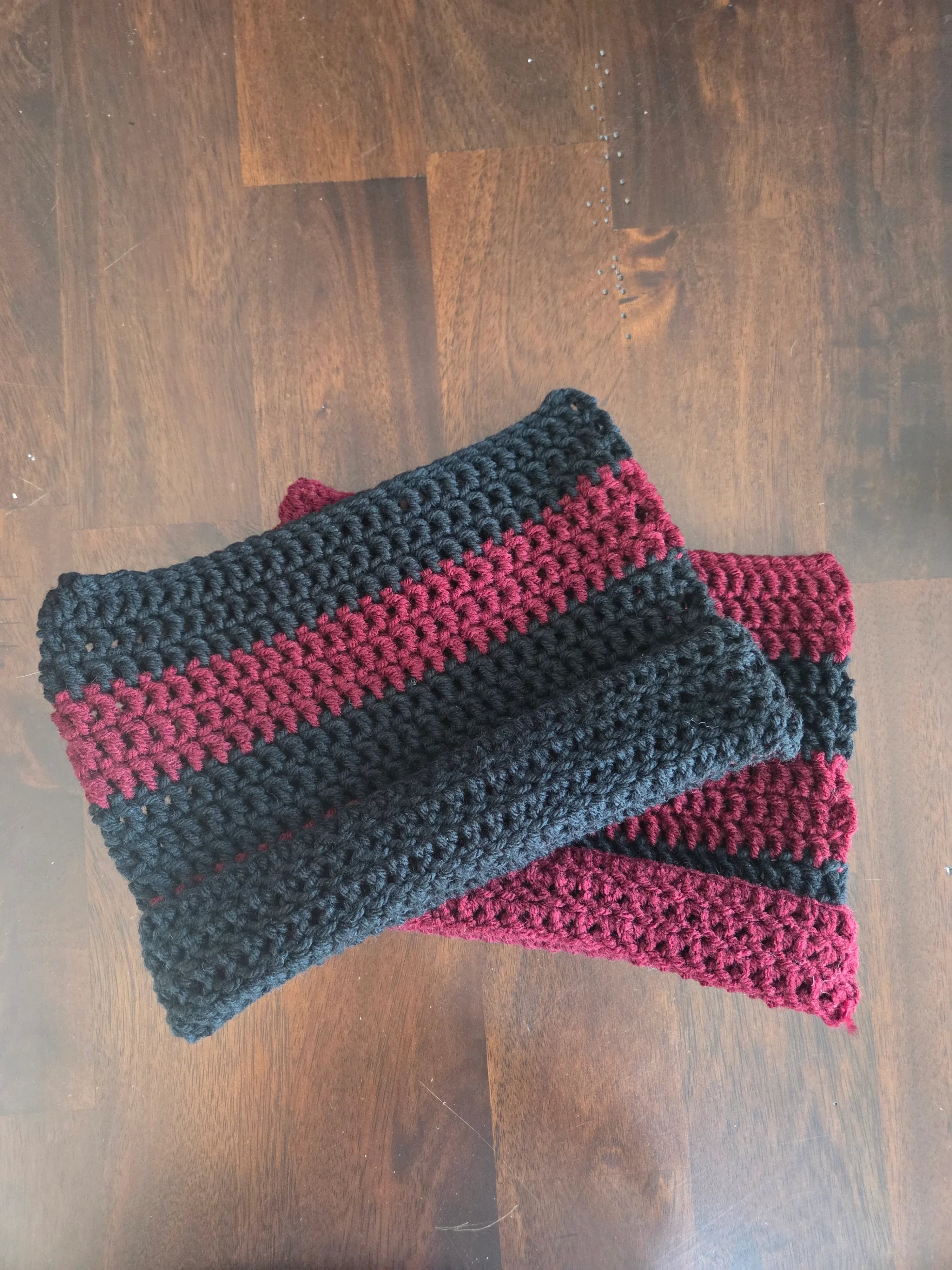Handmade crochet scarf with black and burgundy stripes on a wooden table