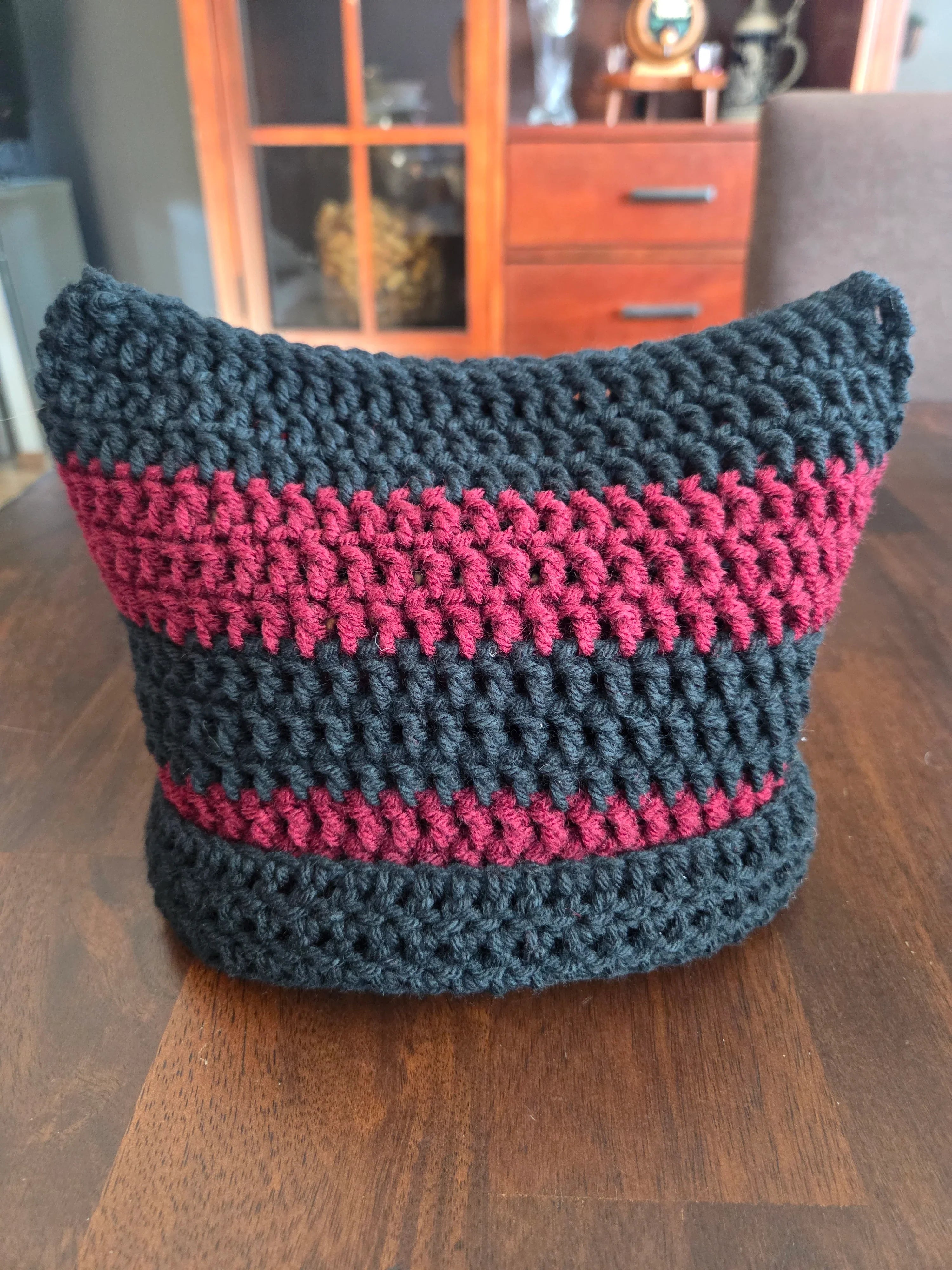 Handmade crochet cat ear hat with black and burgundy stripes on a wooden table
