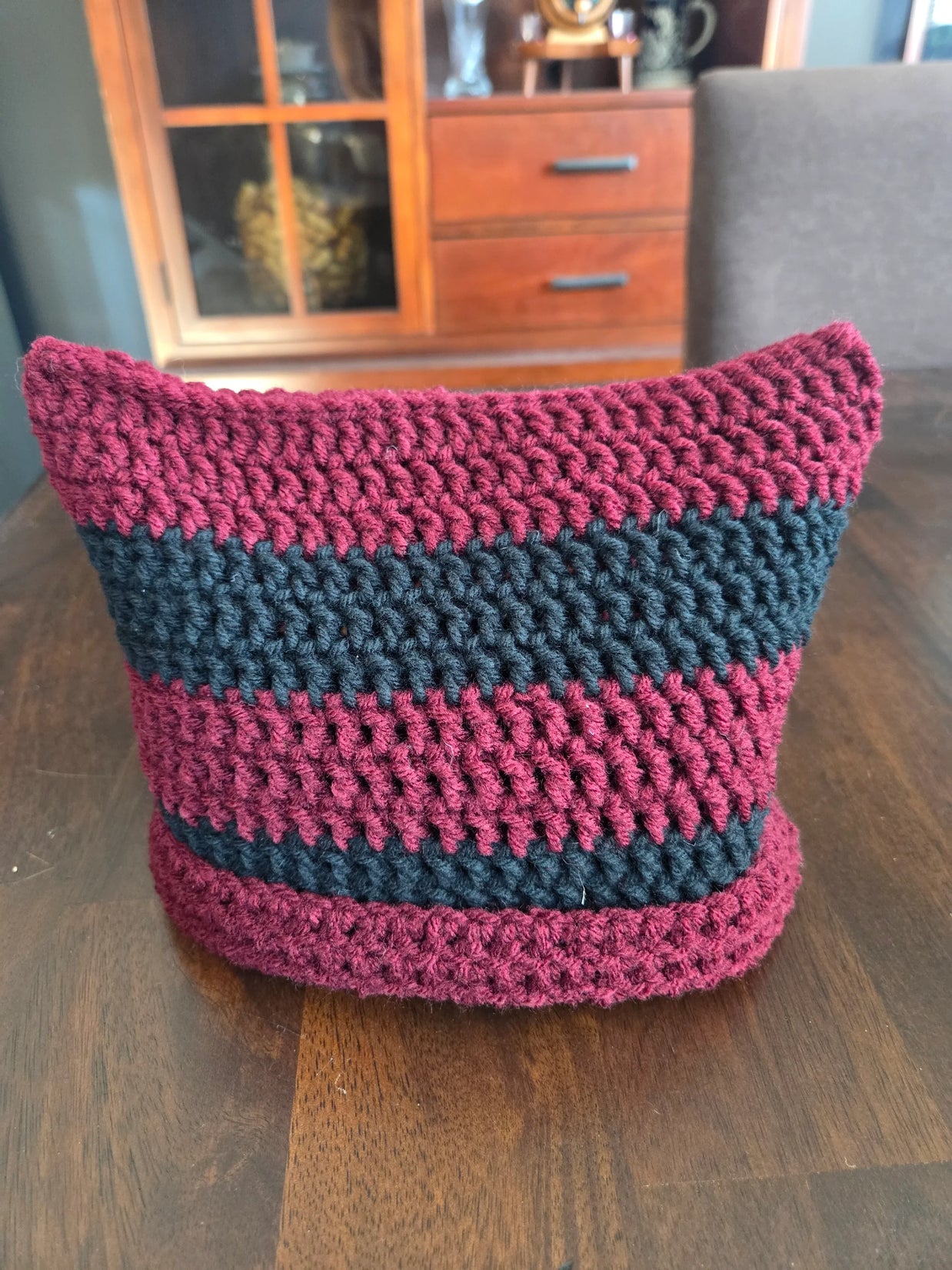 Handmade crochet basket with maroon and black stripes on a wooden table