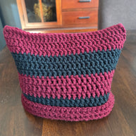 Handmade crochet basket with maroon and black stripes on a wooden table