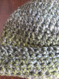 Close-up of a green and gray crochet beanie hat with textured yarn on a wooden surface.