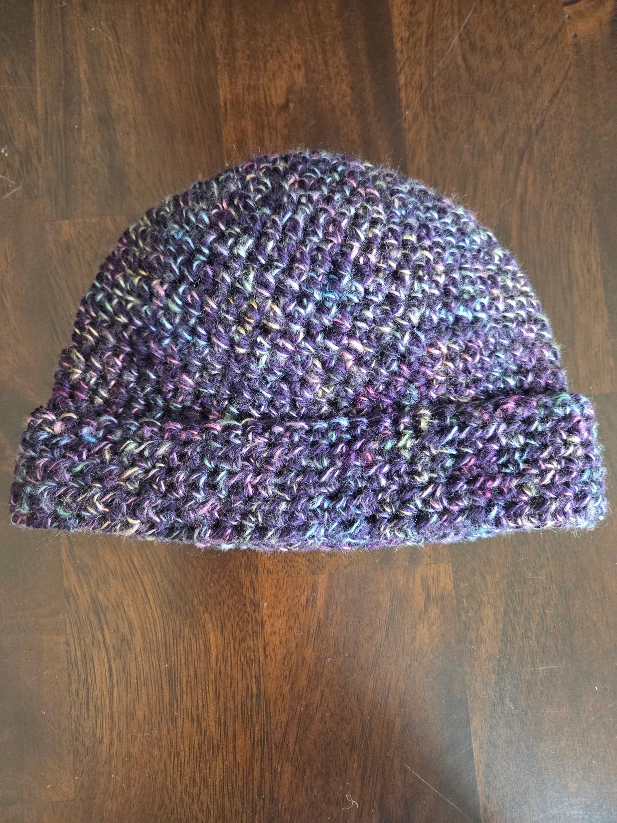 Handmade multicolor knit beanie hat on dark wood surface