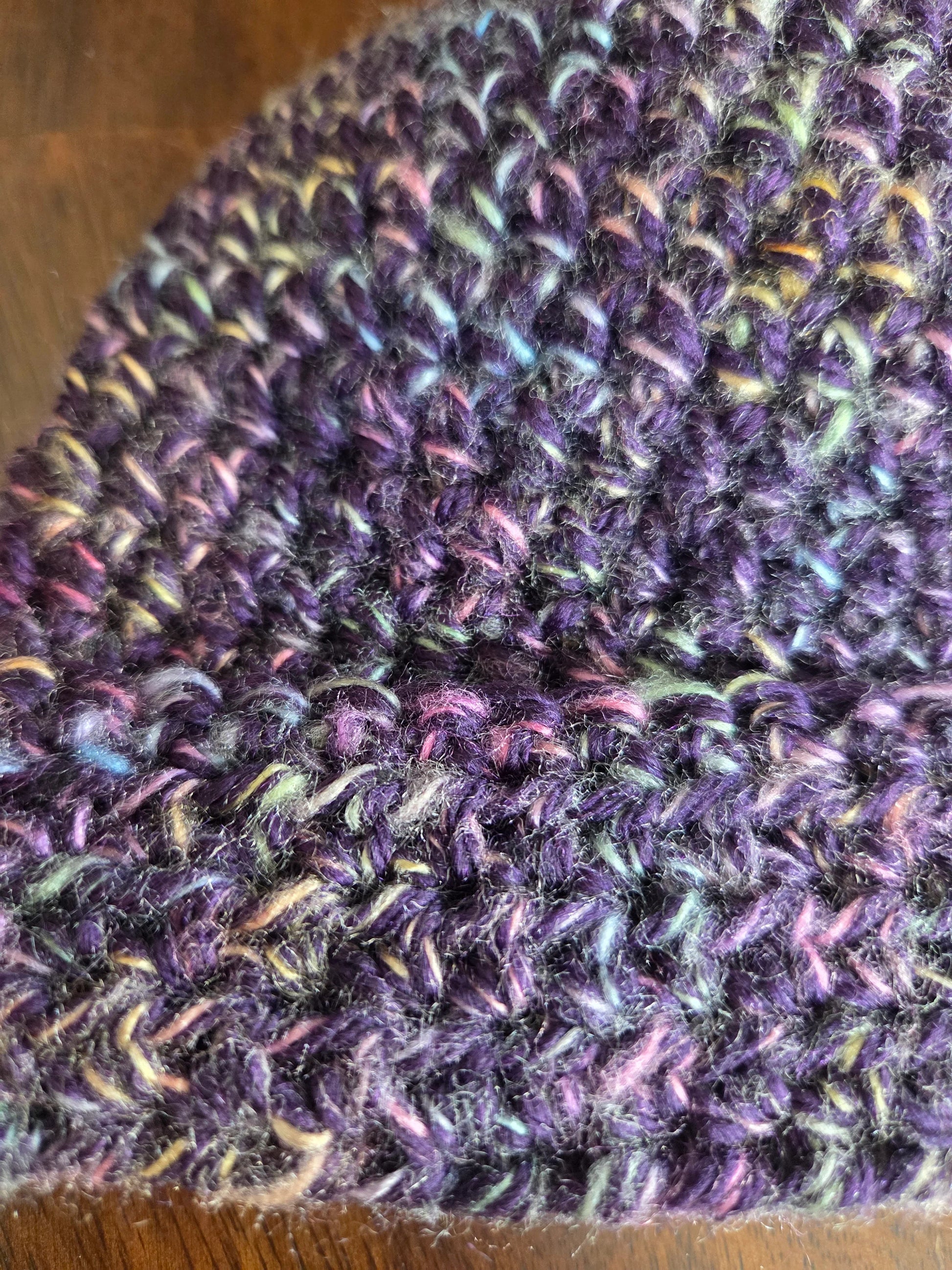 Close-up of a purple knitted hat with multicolored yarn detail on a wooden surface