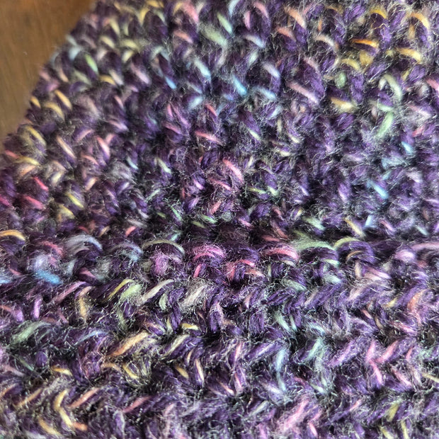 Close-up of a purple knitted hat with multicolored yarn detail on a wooden surface