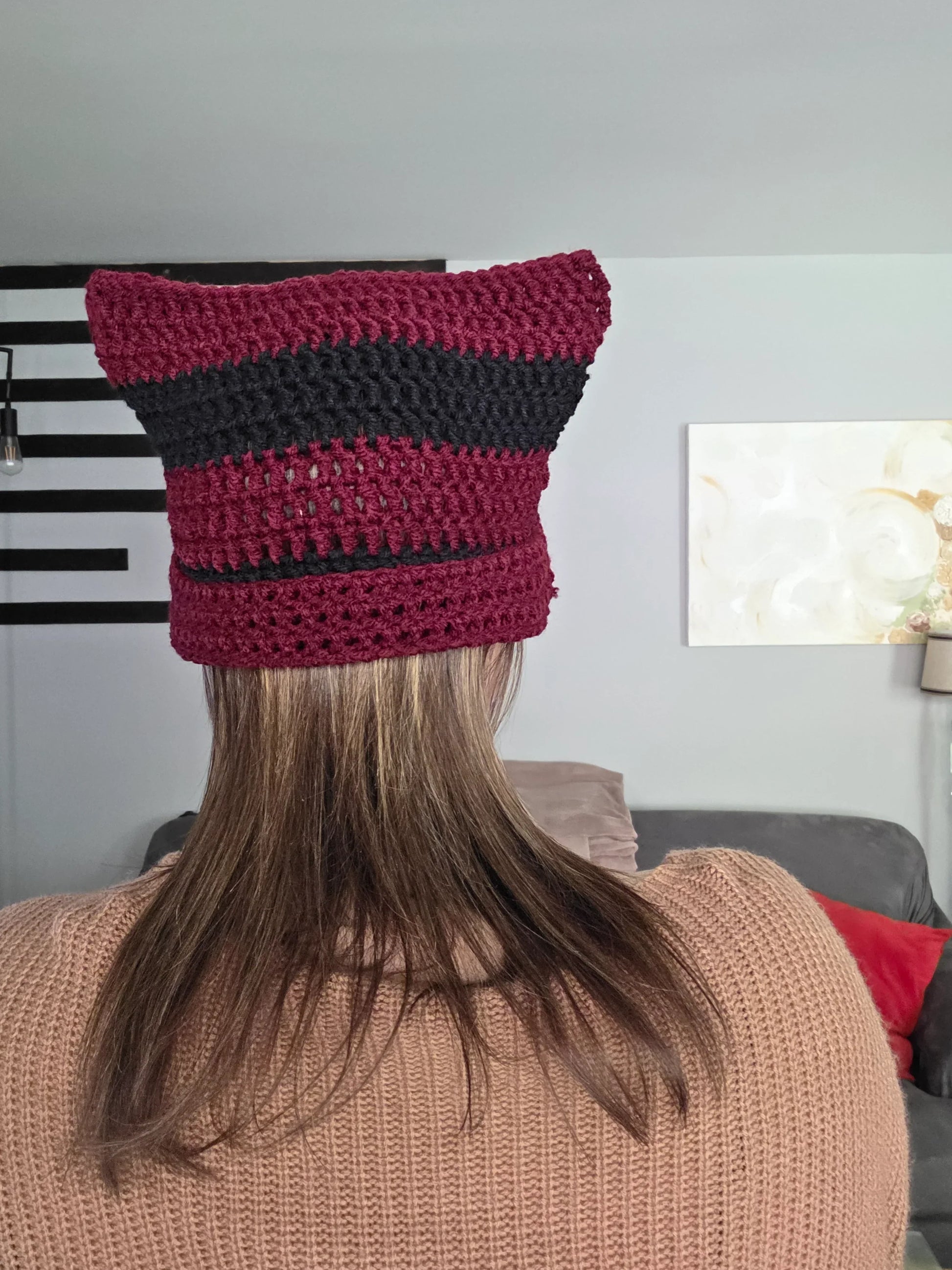 Woman wearing a handmade maroon and black crochet cat ear beanie indoors