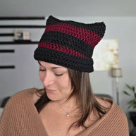 Woman wearing a handmade black and burgundy crochet cat ear beanie indoors