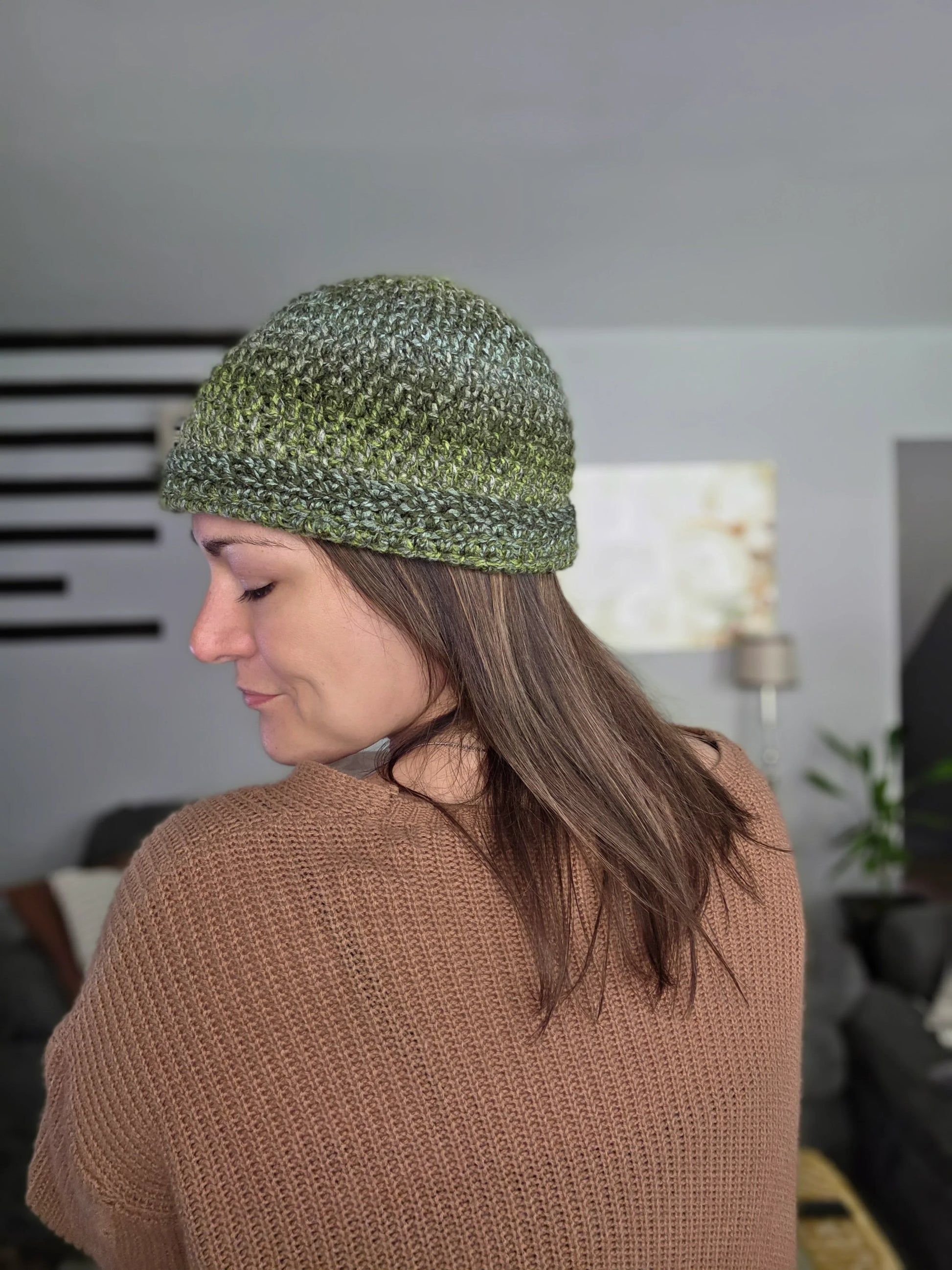 Woman wearing a green crochet beanie and brown knit sweater indoors