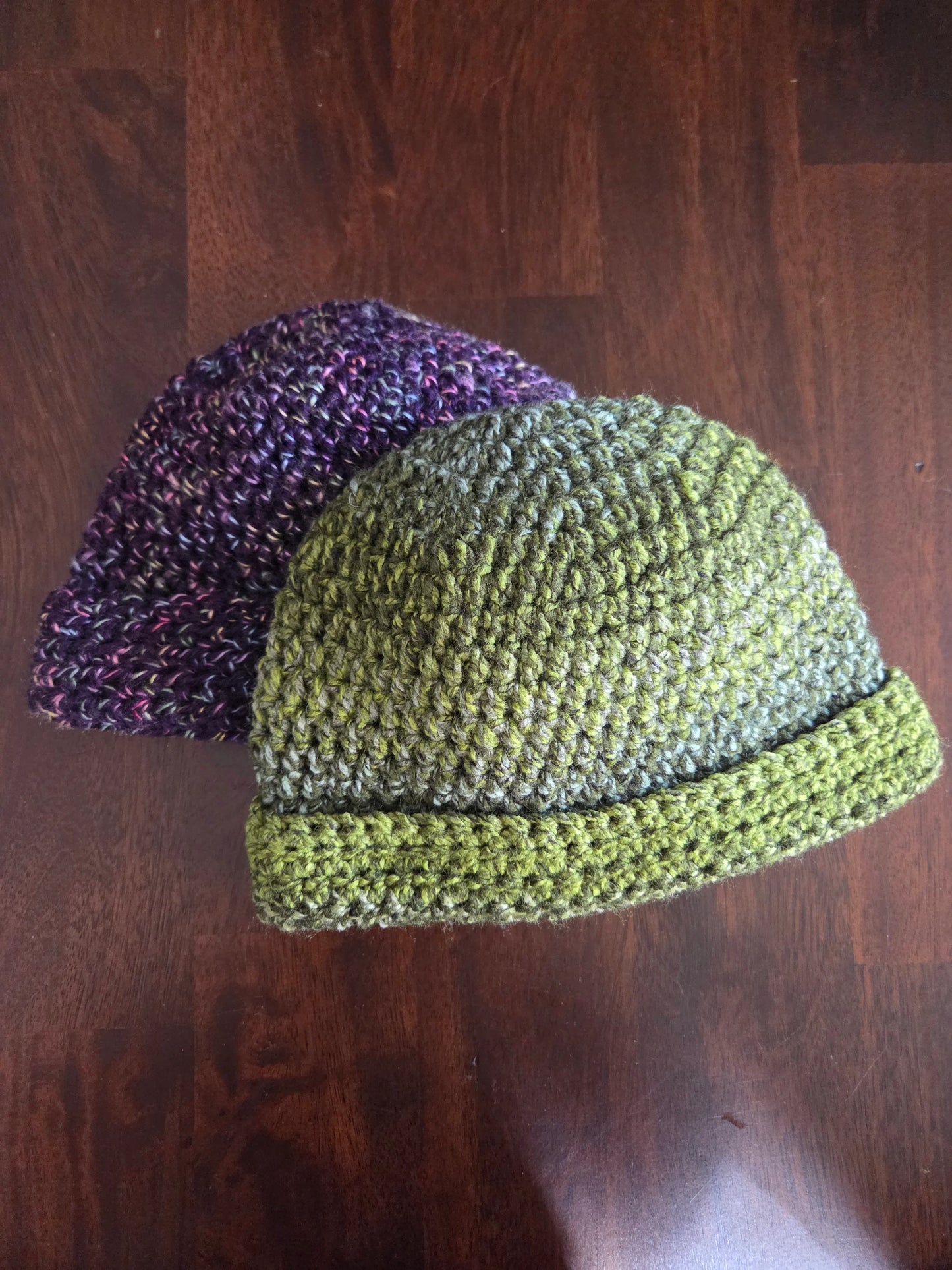 Handmade crochet beanies in green and purple yarn on a wooden surface