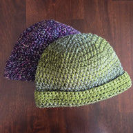 Handmade crochet beanies in green and purple yarn on a wooden surface