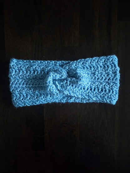 Handmade light blue crochet headband with knot, displayed on a dark wooden surface