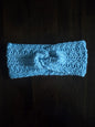 Handmade light blue crochet headband with knot, displayed on a dark wooden surface