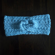 Handmade light blue crochet headband with knot, displayed on a dark wooden surface