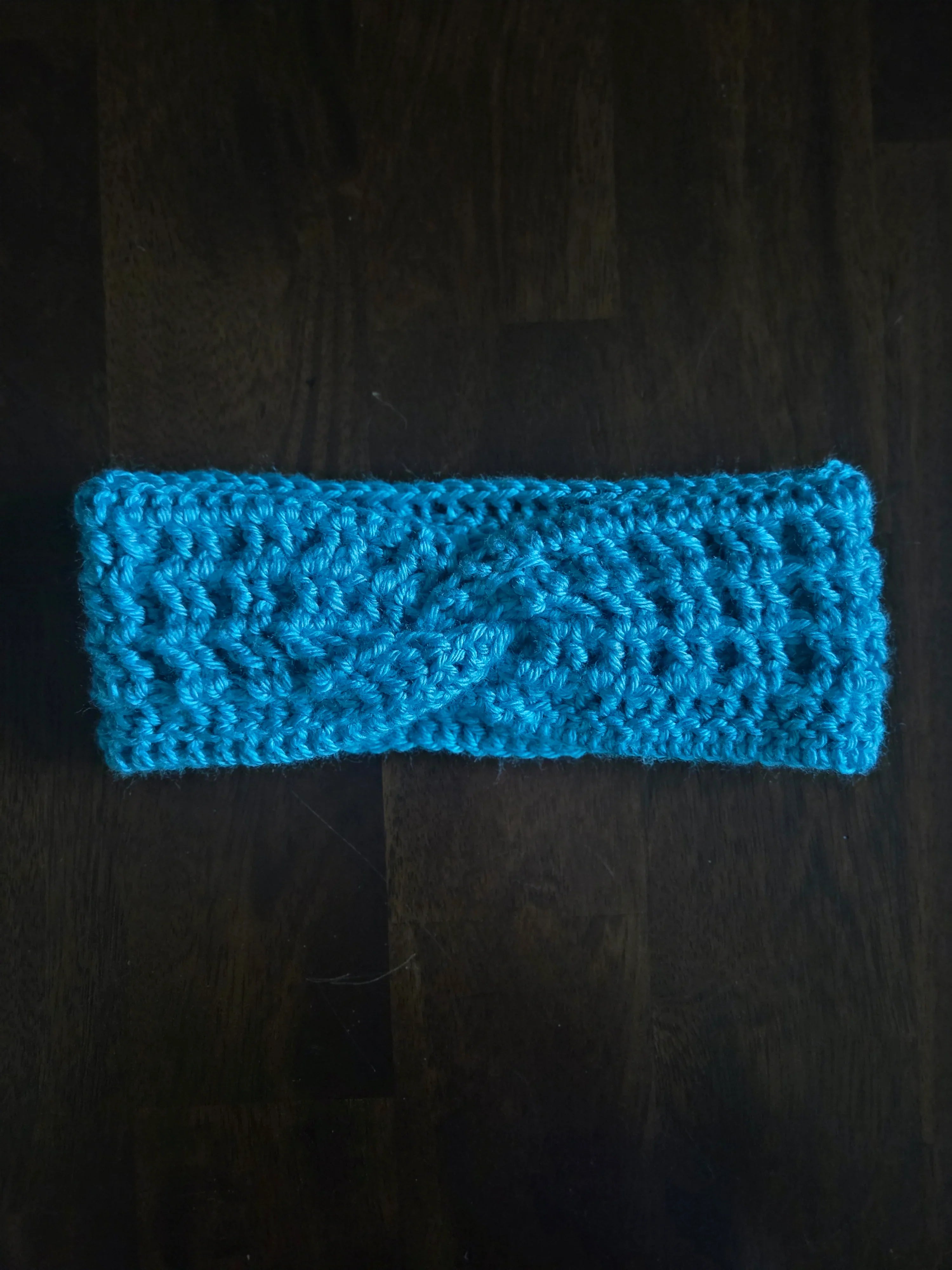 Handmade blue crochet headband with twist detail on dark wooden surface