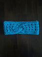 Handmade blue crochet headband with twist detail on dark wooden surface