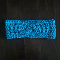 Handmade blue crochet headband with twist detail on dark wooden surface