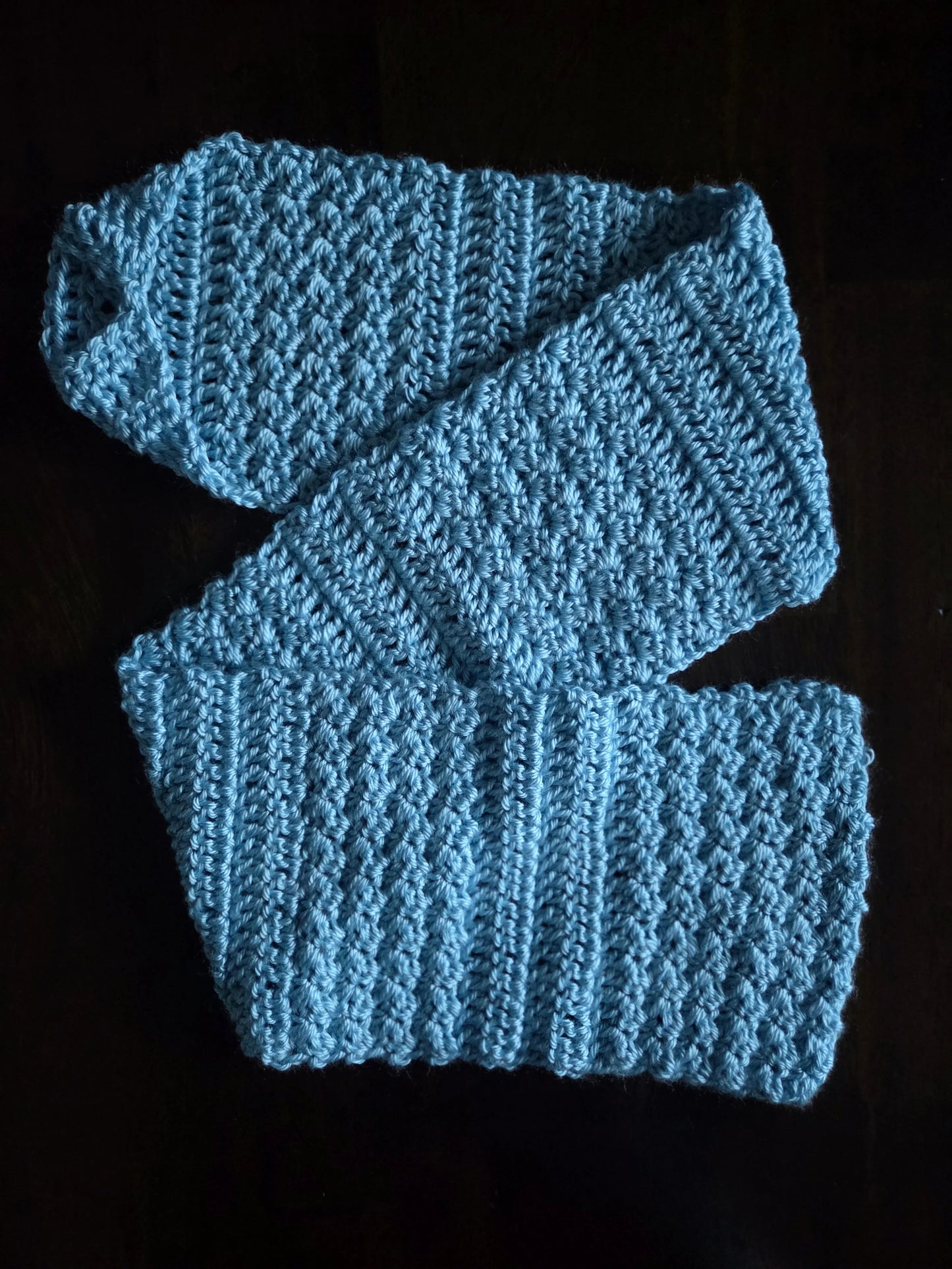 Light blue crocheted scarf with textured stitch pattern on dark background