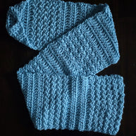 Light blue crocheted scarf with textured stitch pattern on dark background