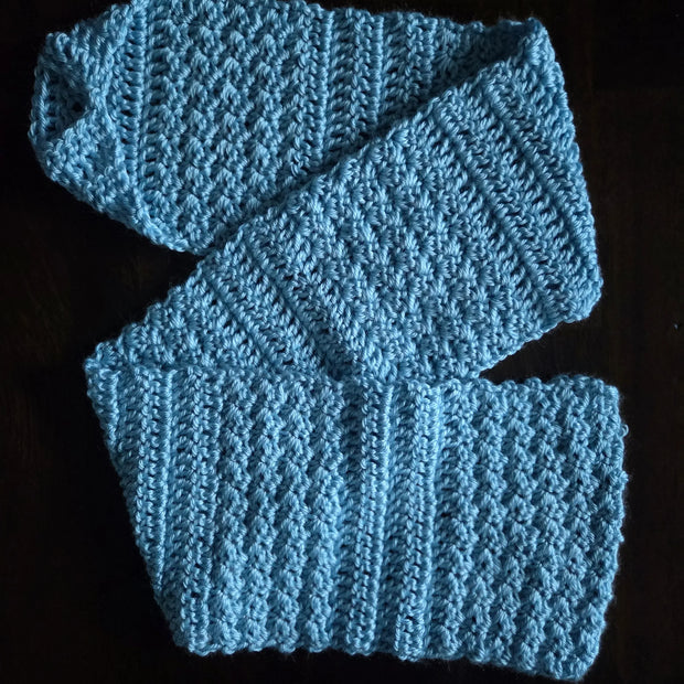 Light blue crocheted scarf with textured stitch pattern on dark background