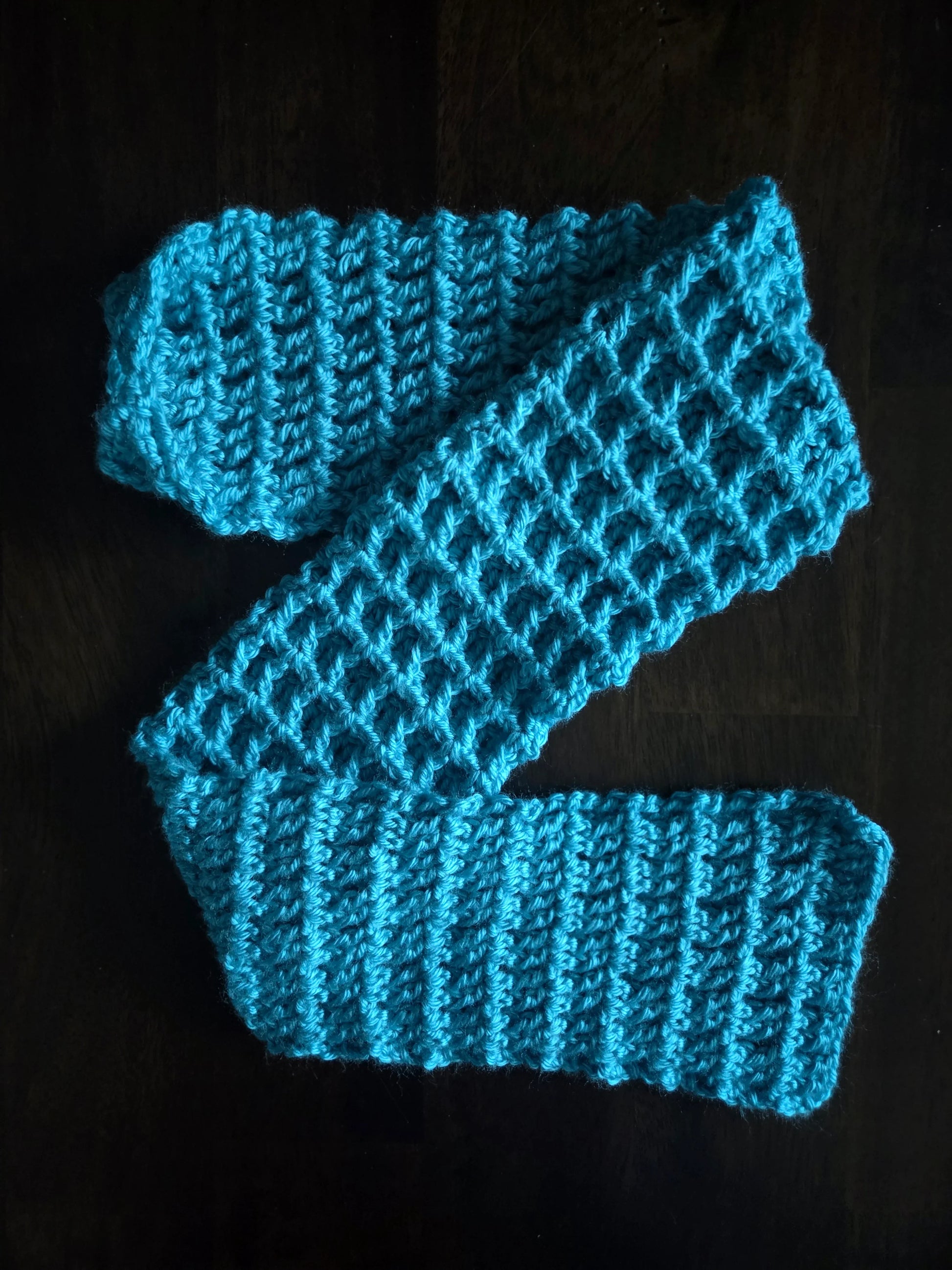 Handmade bright blue crocheted scarf on a dark wooden surface