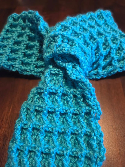 Handmade blue crochet scarf with textured waffle stitch on dark wood background