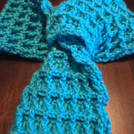 Handmade blue crochet scarf with textured waffle stitch on dark wood background