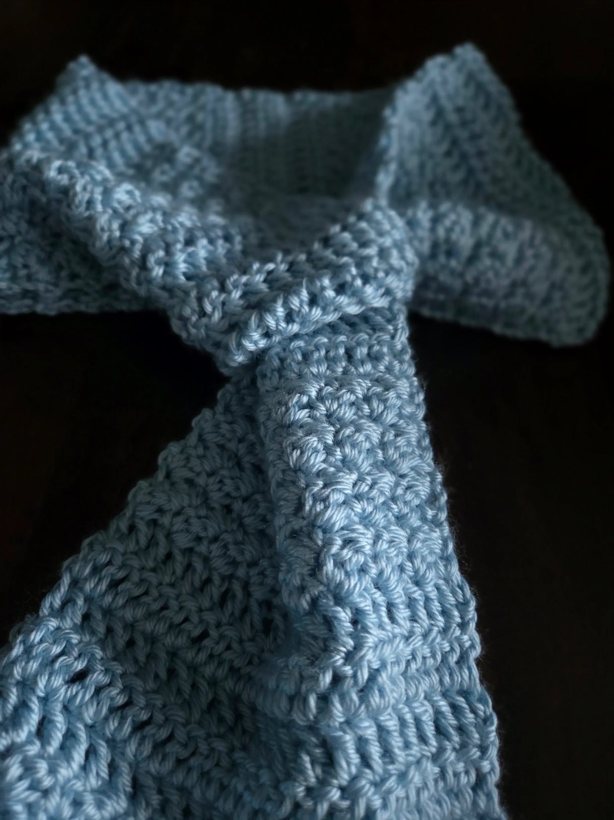 Hand-crocheted blue scarf with textured yarn on a dark background