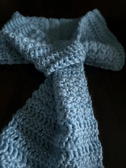 Hand-crocheted blue scarf with textured yarn on a dark background