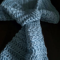 Hand-crocheted blue scarf with textured yarn on a dark background