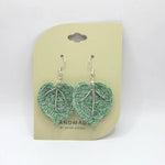 Handmade crochet heart earrings in green and gray, featuring silver beads and hooks, displayed on a pale yellow card.