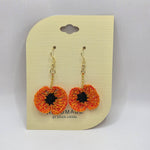 Handmade crochet poppy flower earrings with gold hooks, vibrant orange and yellow petals, black center, on display card