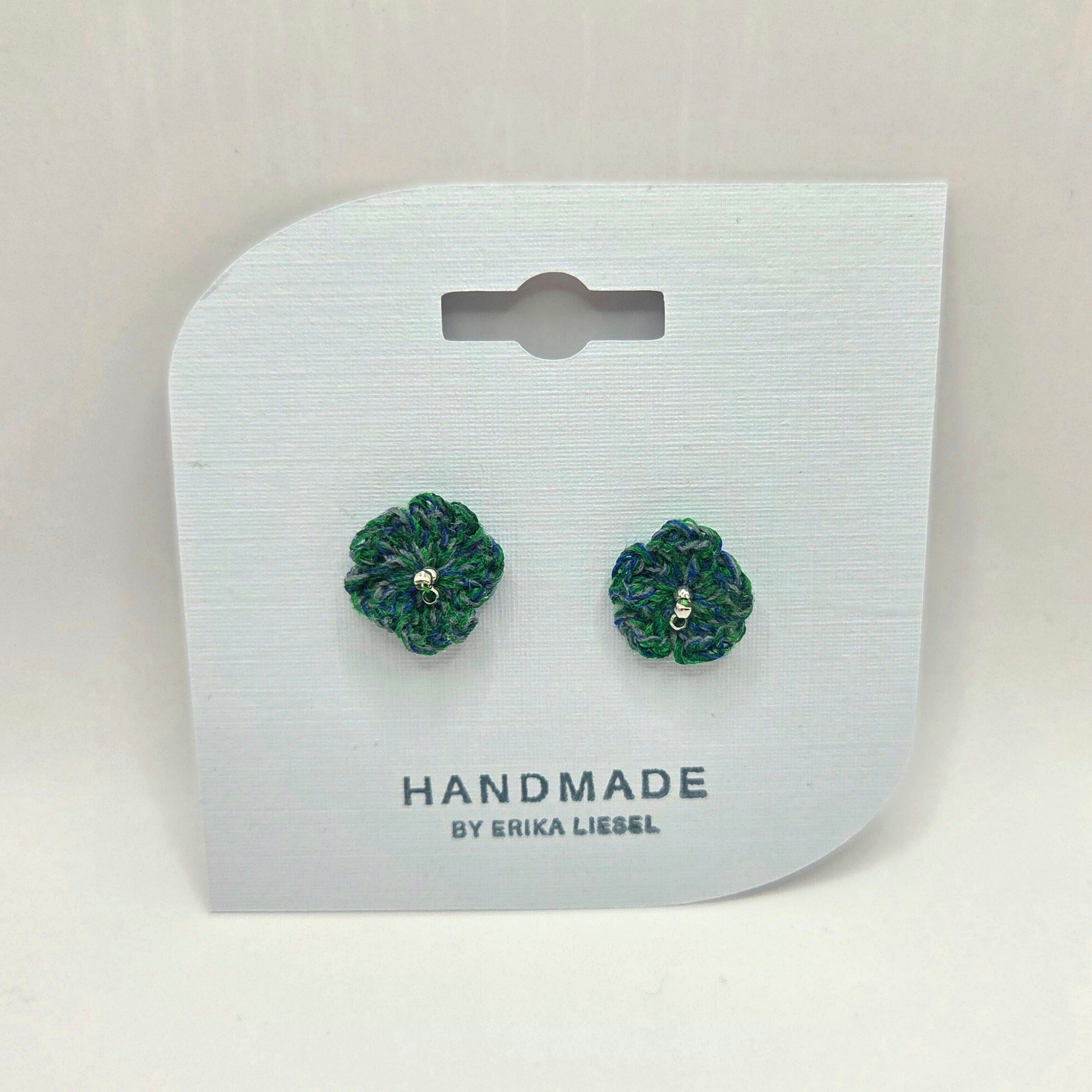 Handmade crochet flower earrings in green and blue, displayed on white card with 'Handmade by Erika Liesel' text.