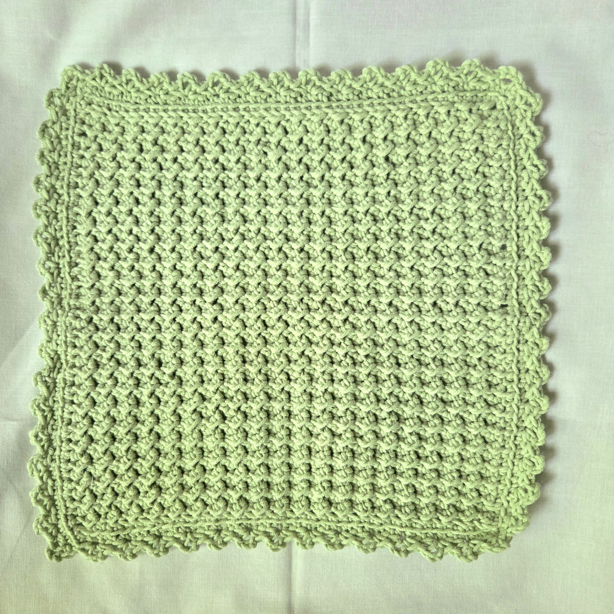 Handmade light green crochet dishcloth with scalloped edges, perfect for cozy kitchen decor or thoughtful gifts.