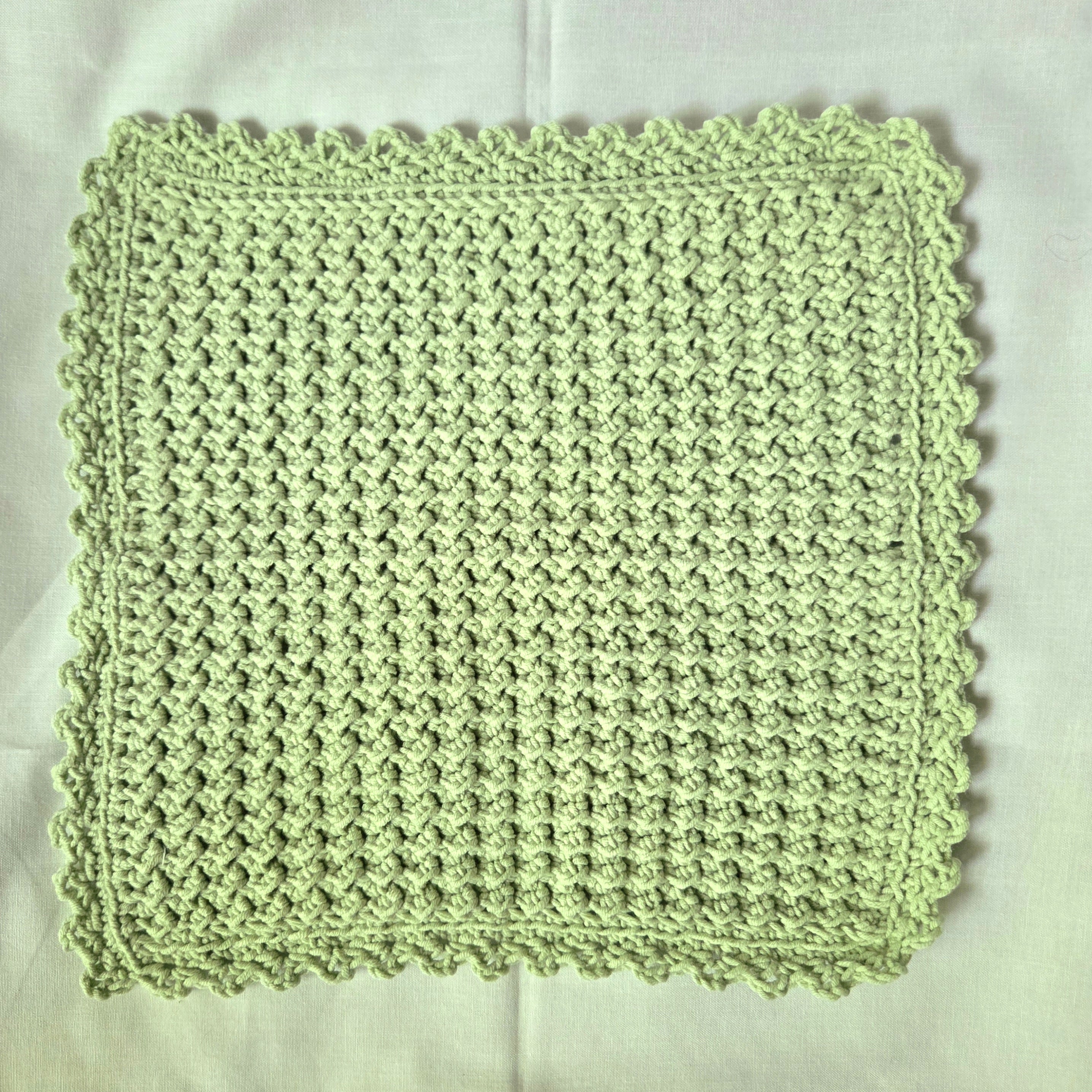 Handmade light green crochet dishcloth with scalloped edges, perfect for cozy kitchen decor or thoughtful gifts.