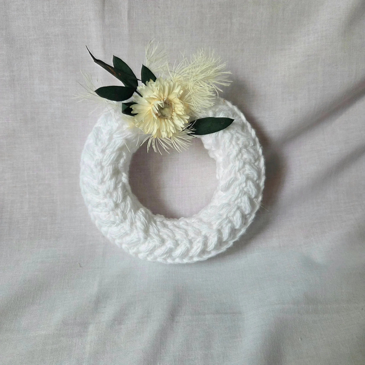 Handmade white crochet wreath with dried flowers and green leaves, cozy home decor