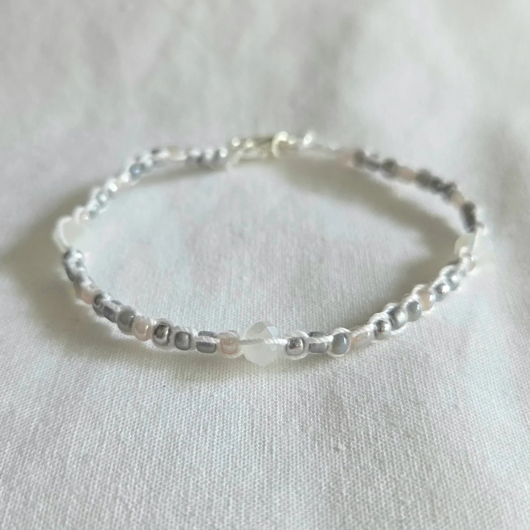 Delicate beaded bracelet with silver, white, and gray beads on white fabric, handmade jewelry gift