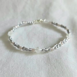 Delicate beaded bracelet with silver, white, and gray beads on white fabric, handmade jewelry gift