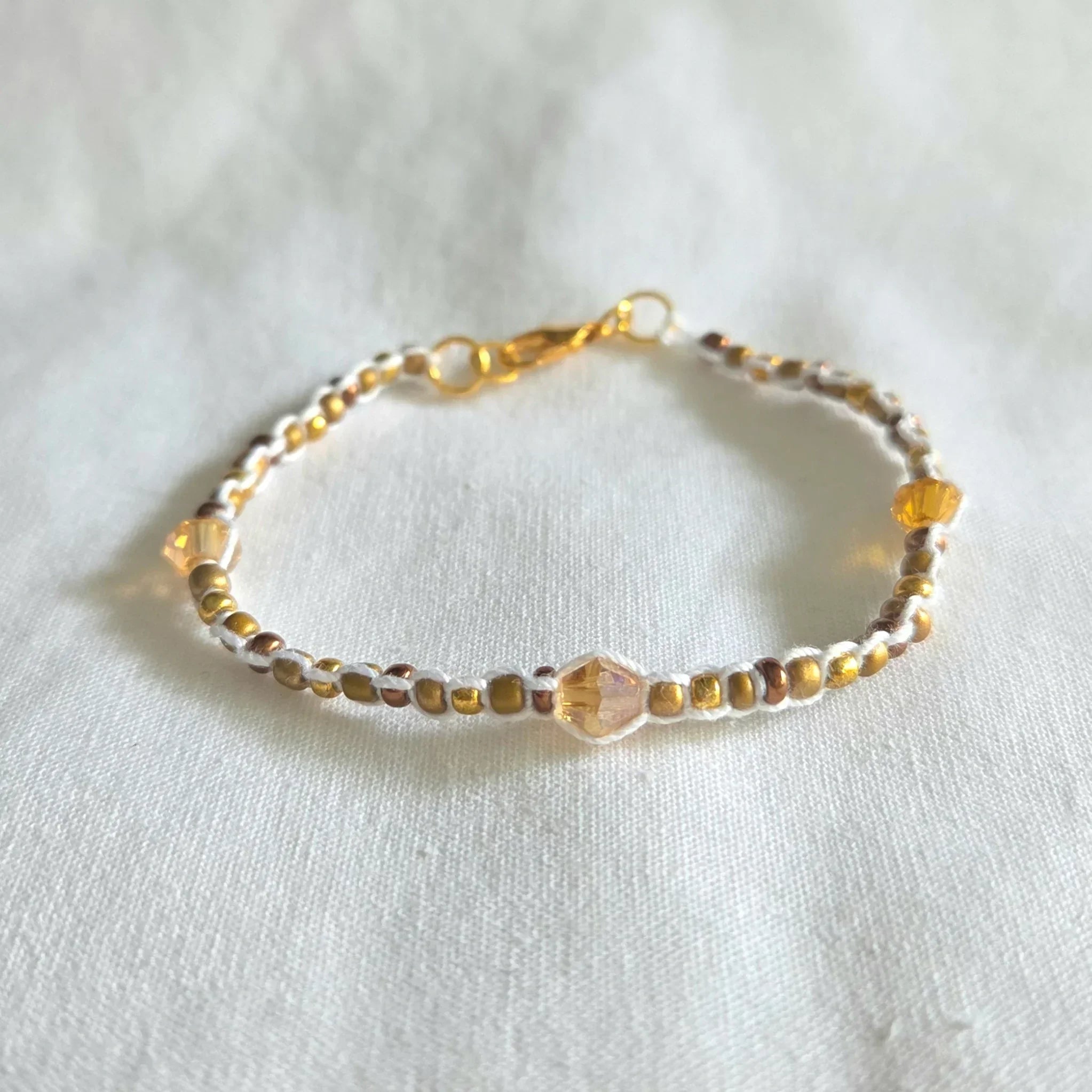 Handmade beaded bracelet with gold, amber, and white beads on white fabric background