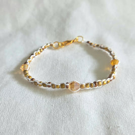 Handmade beaded bracelet with gold, amber, and white beads on white fabric background