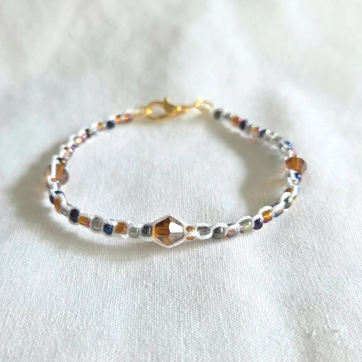 Handmade beaded bracelet with colorful crystals and gold clasp on white fabric