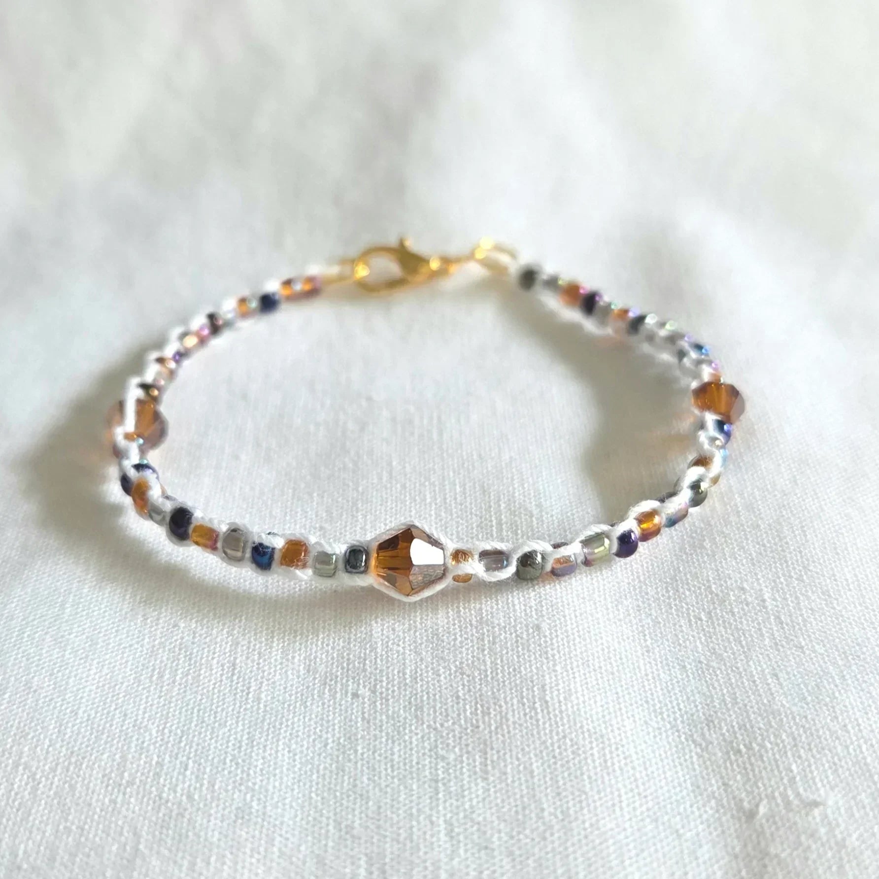Handmade beaded bracelet with colorful crystals and gold clasp on white fabric