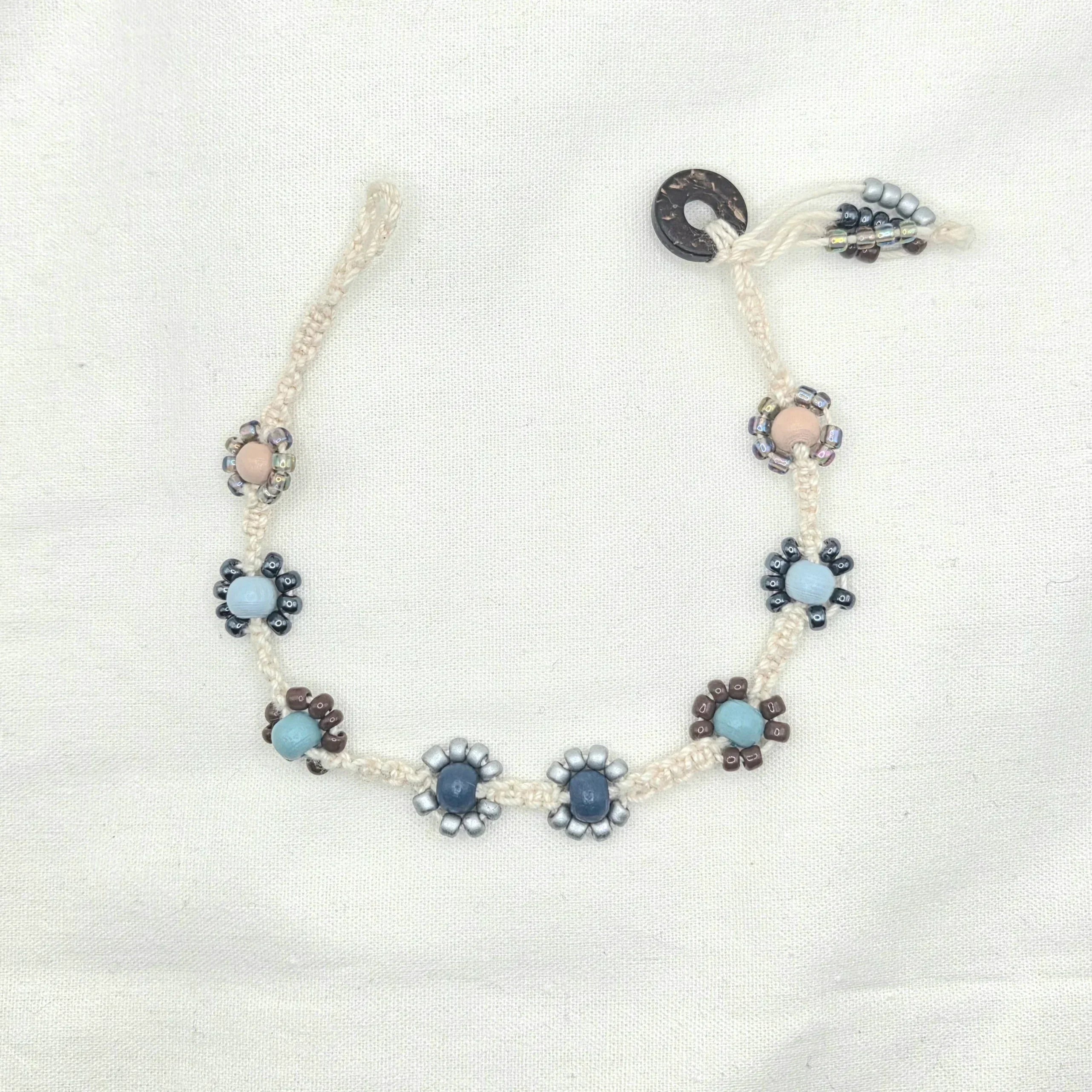 Handmade macrame necklace with beaded flower accents in blue, gray, and brown tones on cream cord