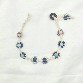 Handmade macrame necklace with beaded flower accents in blue, gray, and brown tones on cream cord