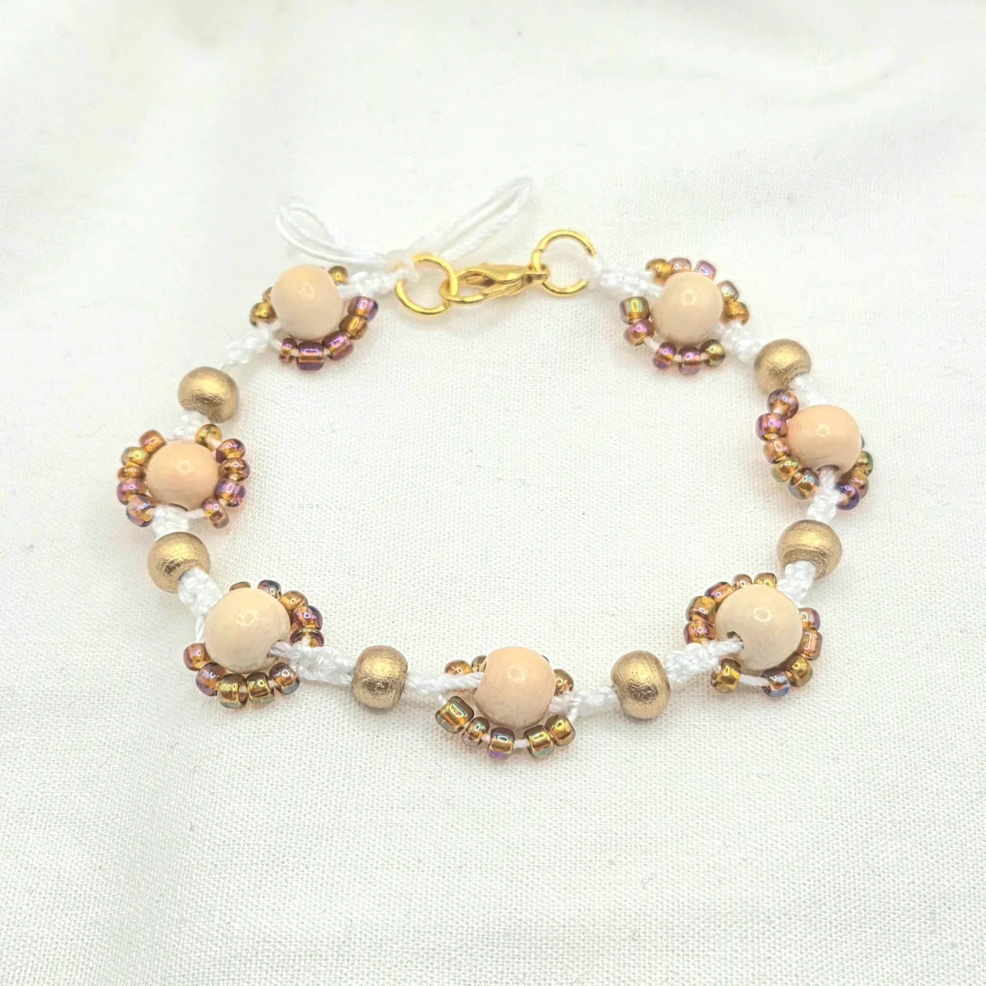 Handmade beaded bracelet with cream wood beads, gold accents, and iridescent seed beads on white cord
